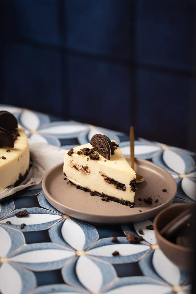 food photography of a slice of Oreo cheesecake on a dark blue background