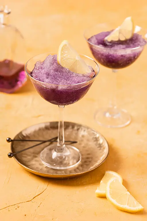 Food photography of glasses filled with purple slush on a yellow background
