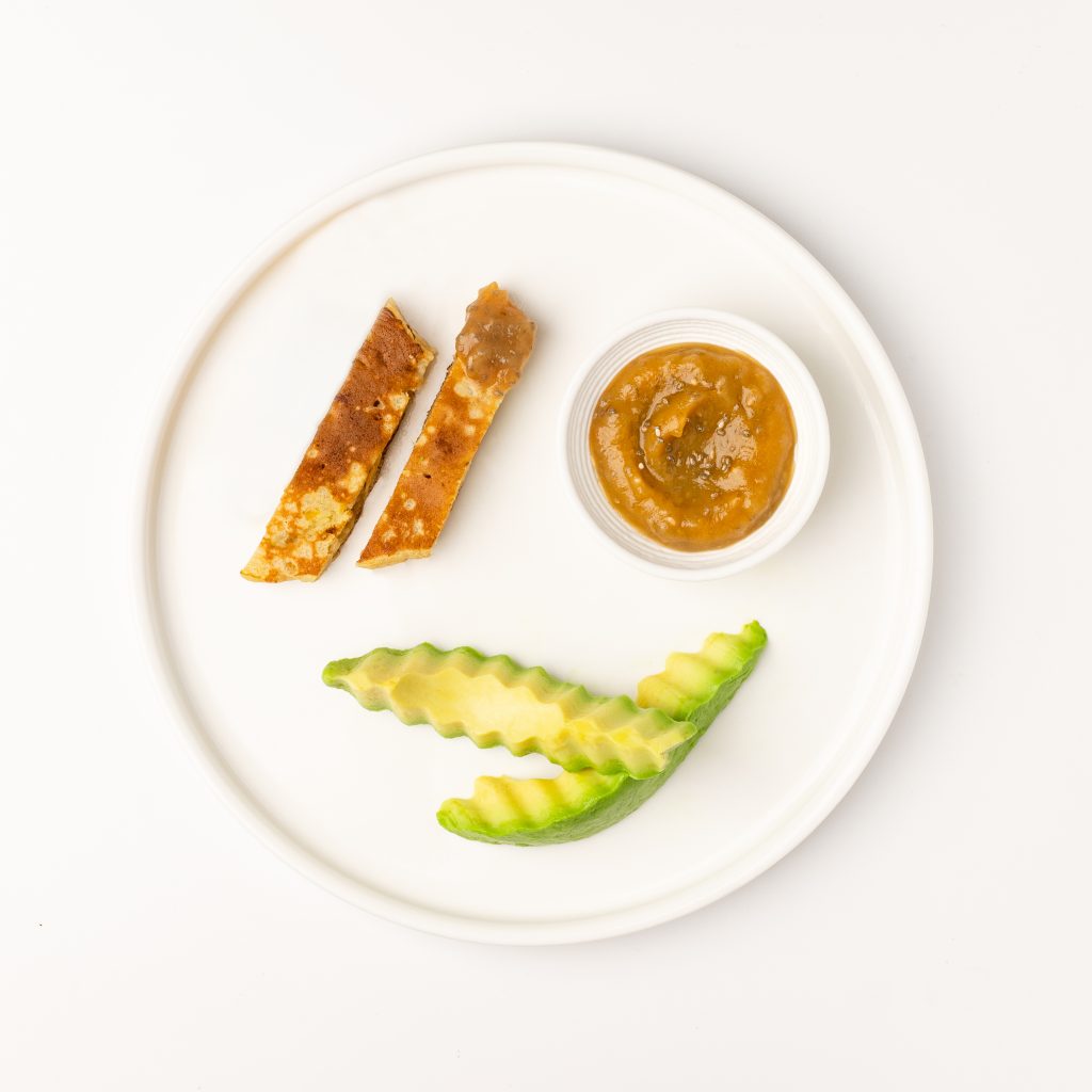 BLW-style breakfast for a child served on a white plate with pancake strips, applesauce, and avocado