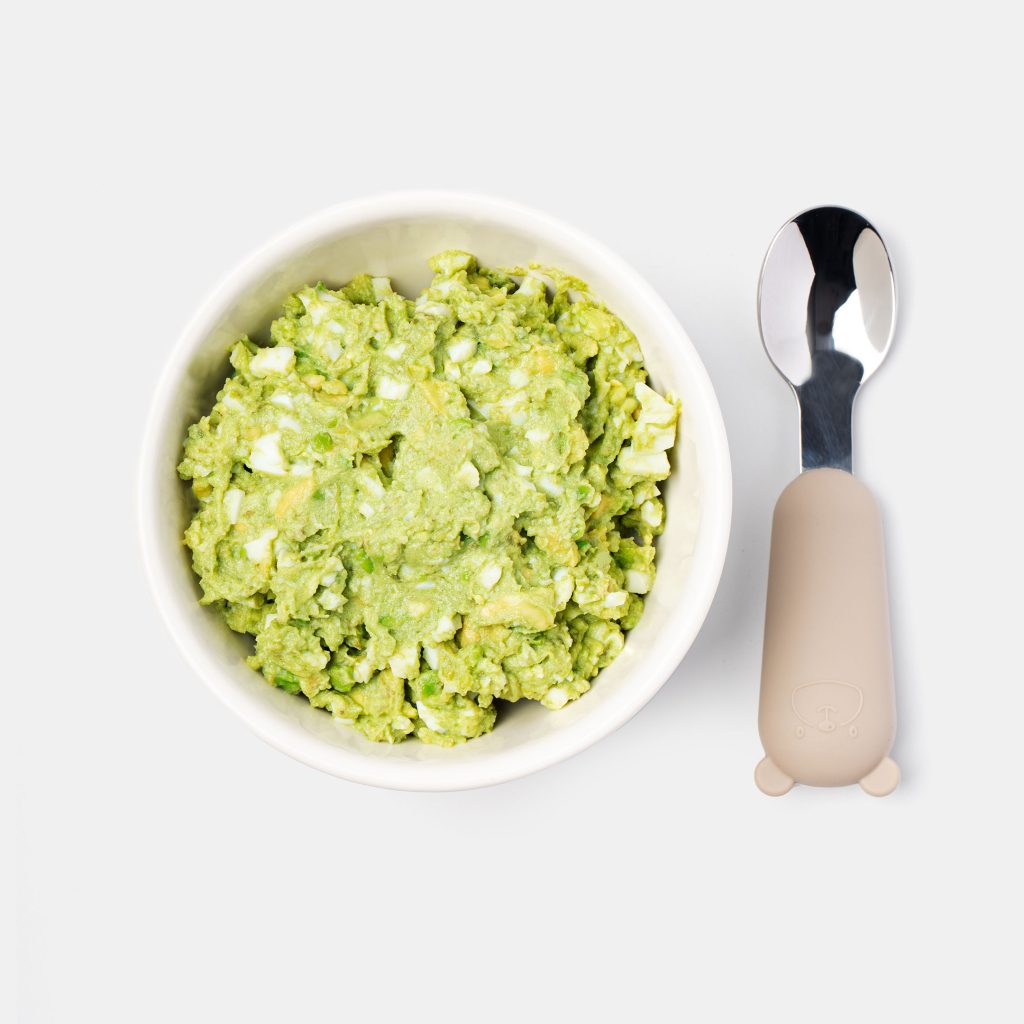 Green pea and egg purée in a bowl with a spoon beside it
