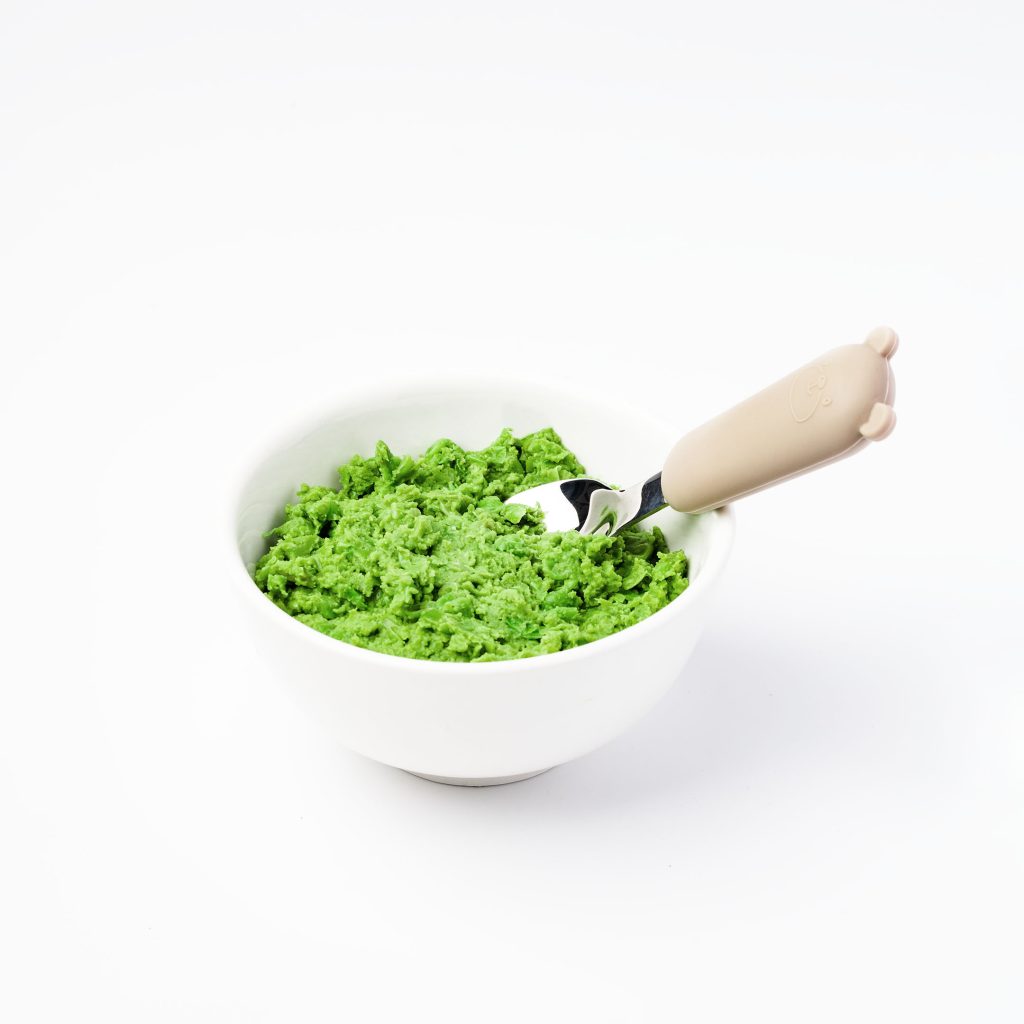 Green pea purée in a bowl with a spoon beside it