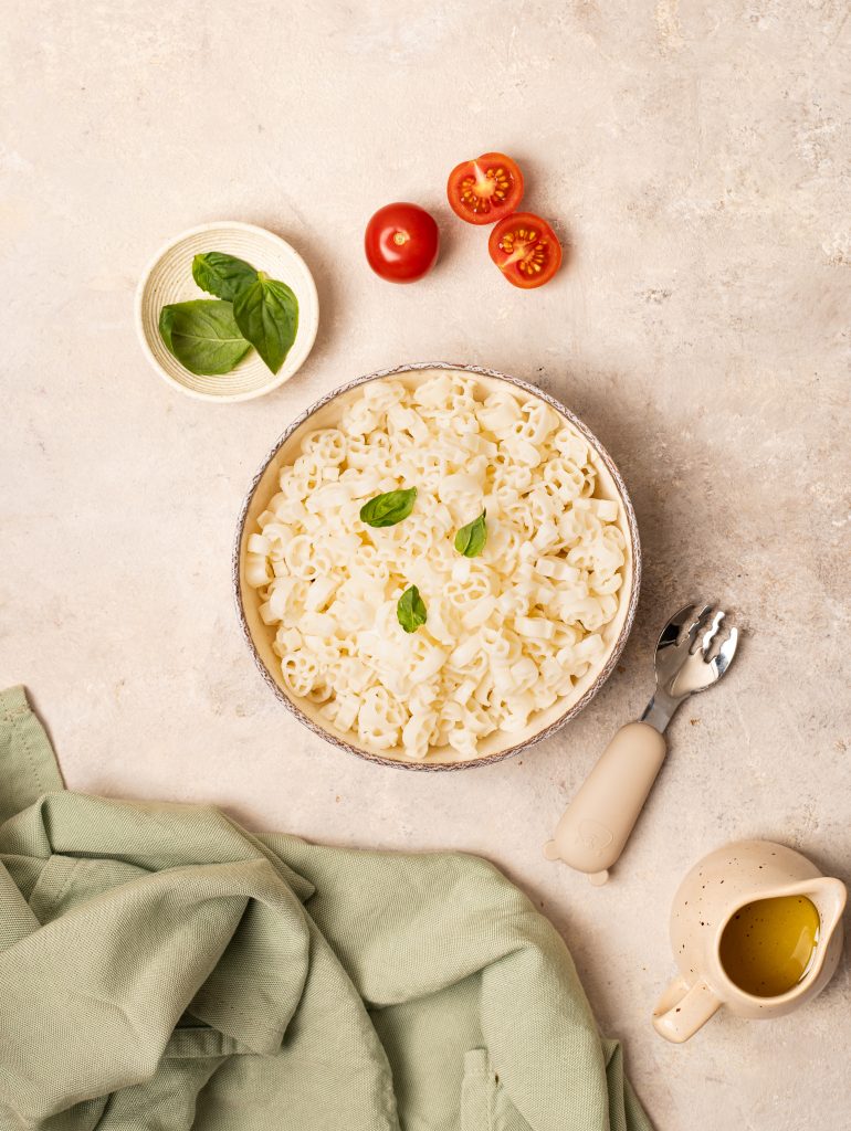 top view of cooked rice pasta in a bowl on a beige background, tomatoes and basil nearby